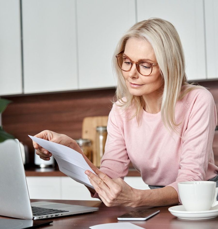 A woman reading through paperwork at her kitchen table